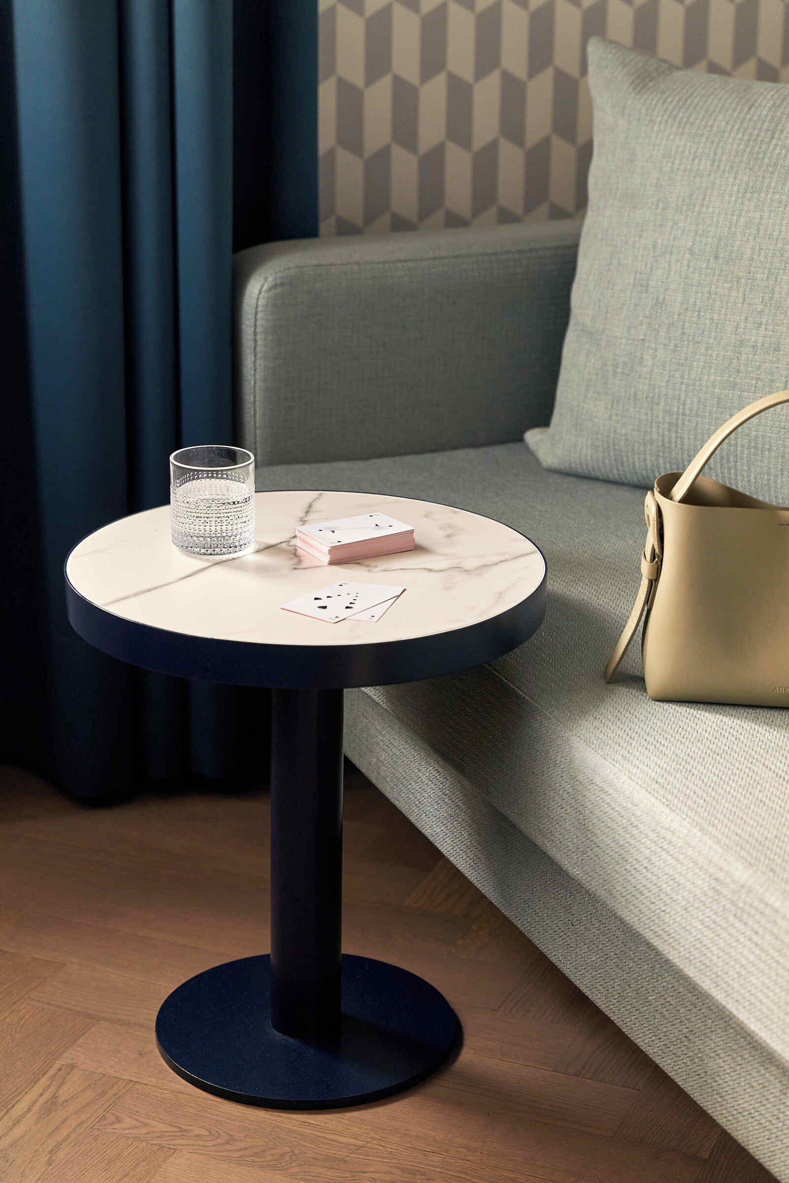 Une table ronde avec un plateau en marbre blanc, un verre d’eau et un jeu de cartes.