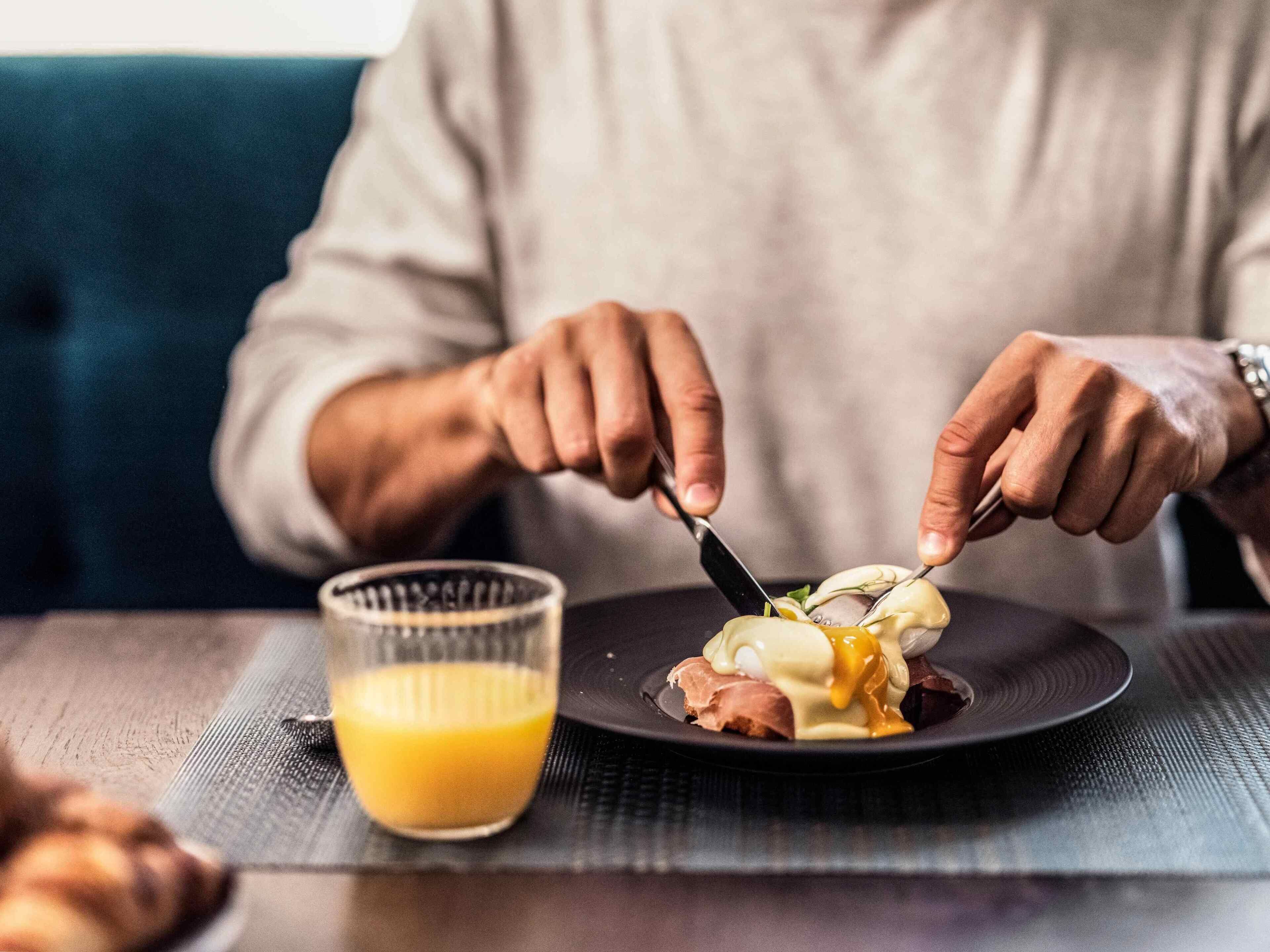 A person eating a breakfast dish with a glass of orange juice on a table.