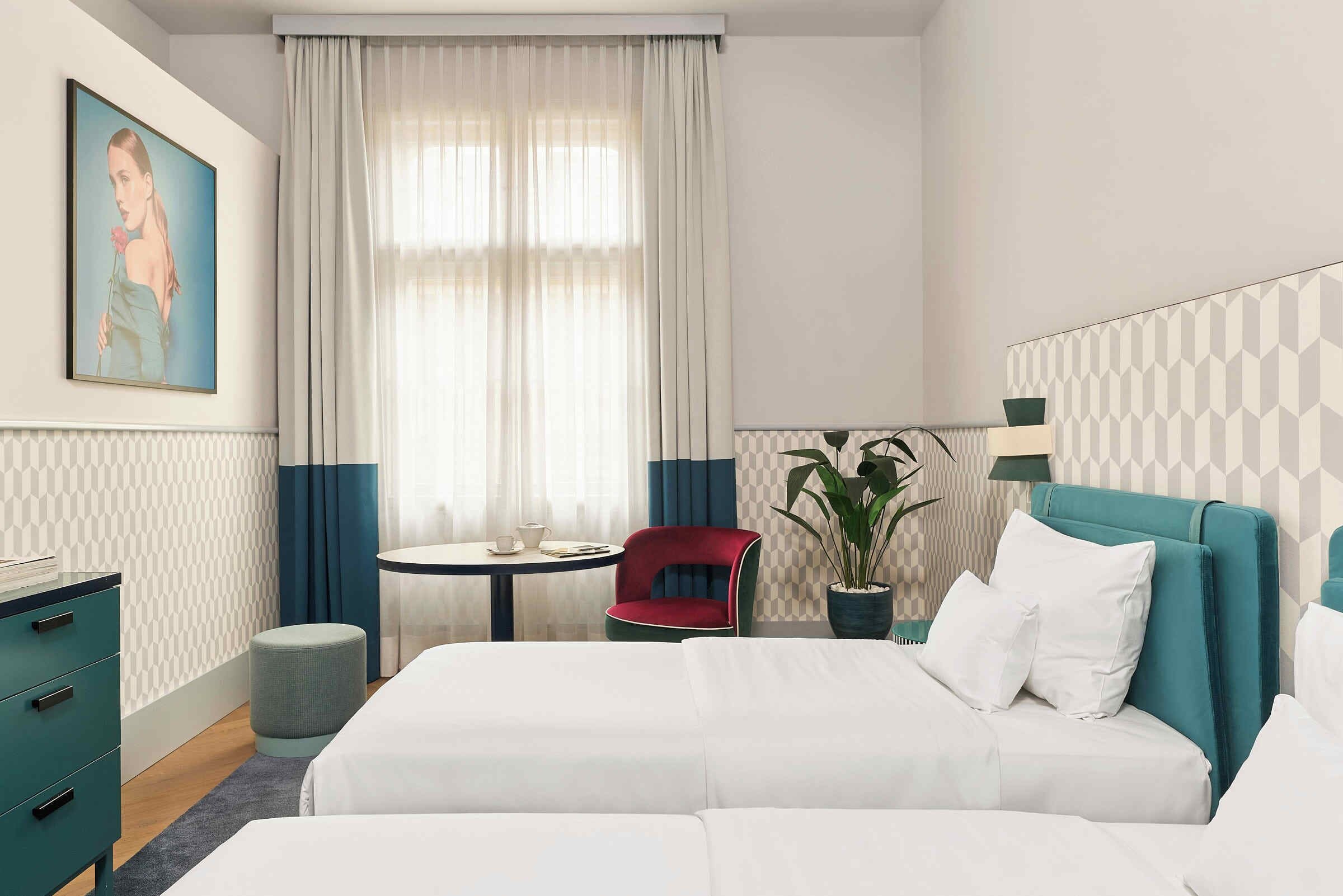 Una habitación de hotel con cama, escritorio, silla, una mesita y una planta en maceta.