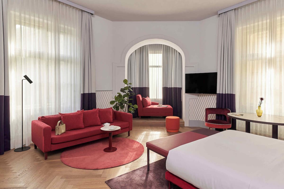 A modern hotel room with a red sofa, a round coffee table, a bed, and a TV.