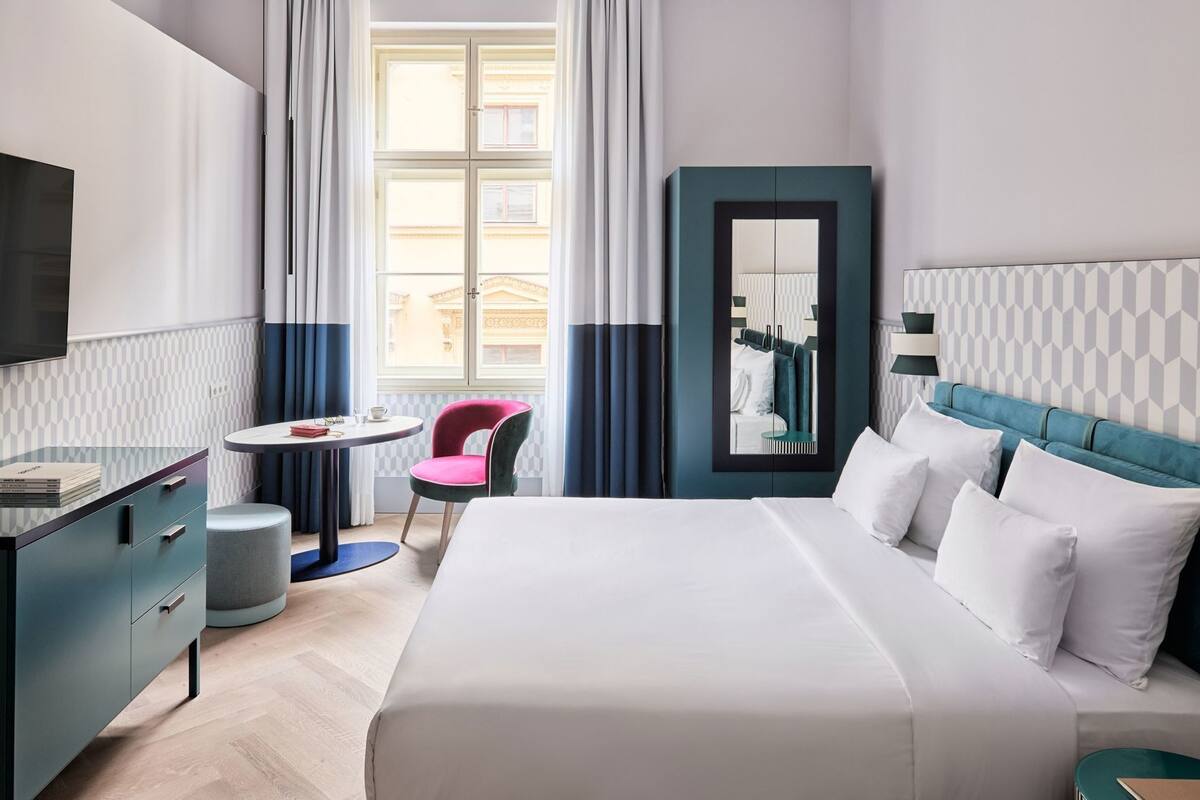 A hotel room with a bed, a desk, a chair, a round table, and a mirror.