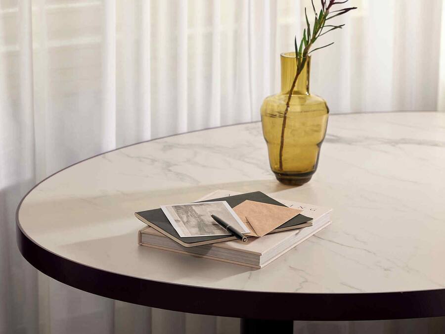 A round table with a marble top, a yellow vase with a red flower, and a stack of magazines.