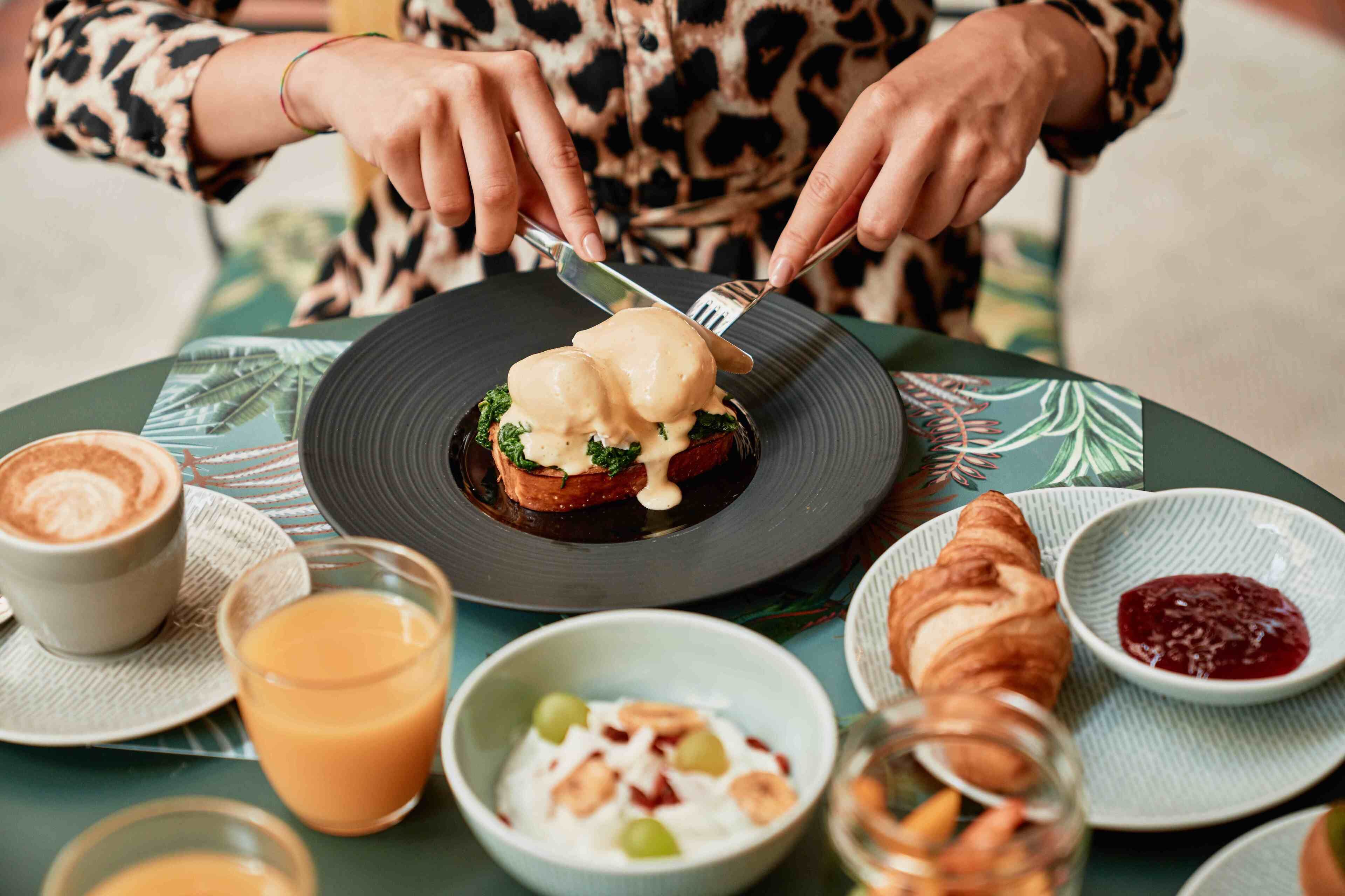 A breakfast setting with a plate of eggs benedict, a croissant, and a glass of orange juice.