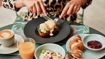 Une table dressée pour le petit-déjeuner avec une assiette d’œufs Bénédicte, un croissant et un verre de jus d’orange.