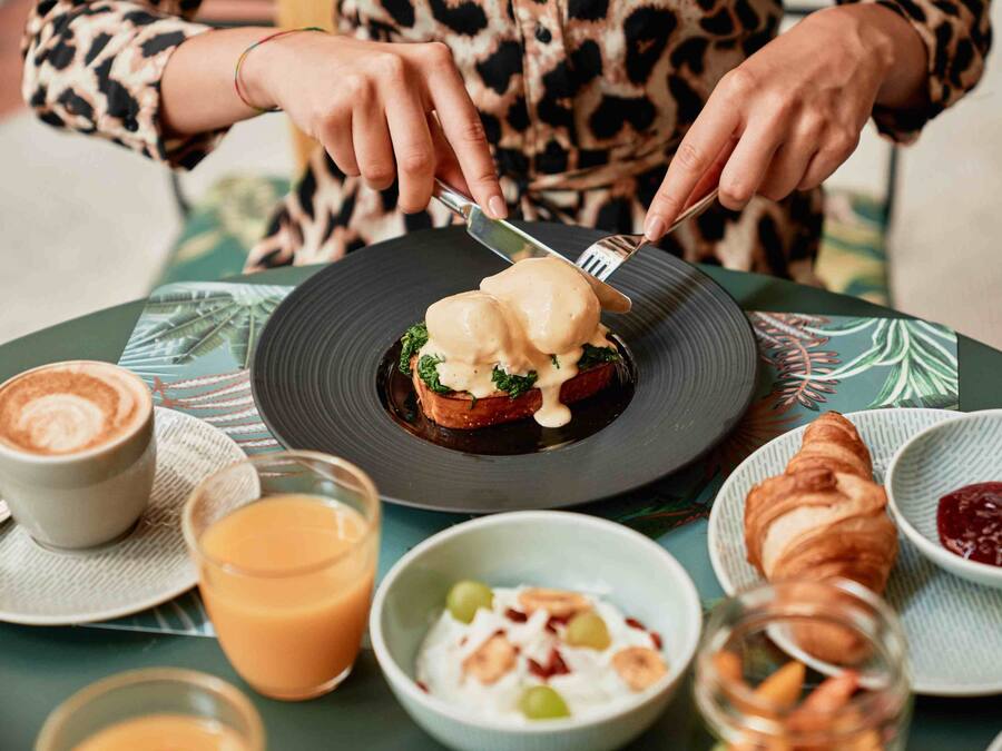 Une table dressée pour le petit-déjeuner avec une assiette d’œufs Bénédicte, un croissant et un verre de jus d’orange.