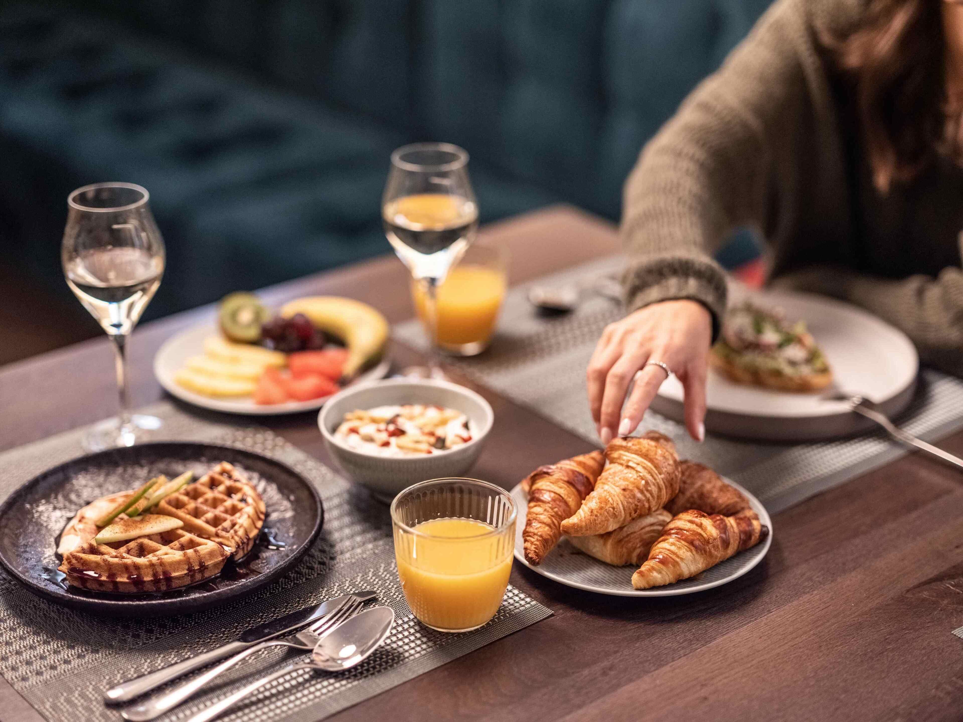 A breakfast setting with waffles, croissants, fruit, and juice on a table.