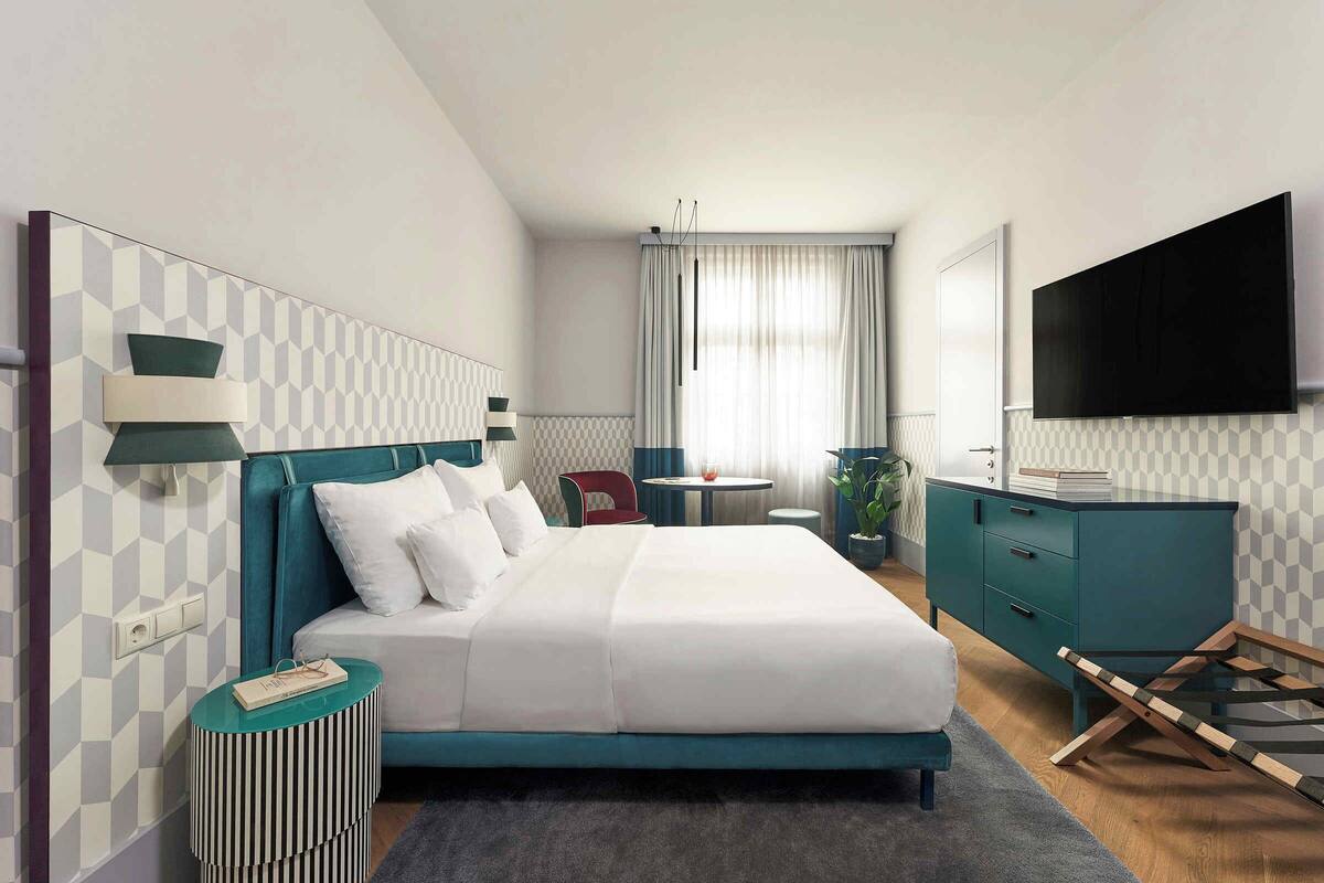 A modern hotel room with a large bed, a TV, a desk, and a chair.