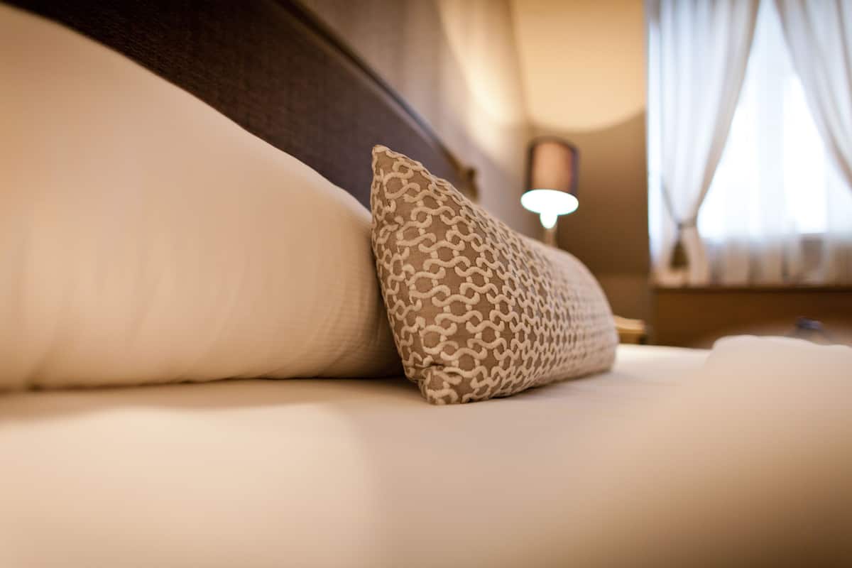 A close-up of a bed with a patterned pillow and a plain pillow.