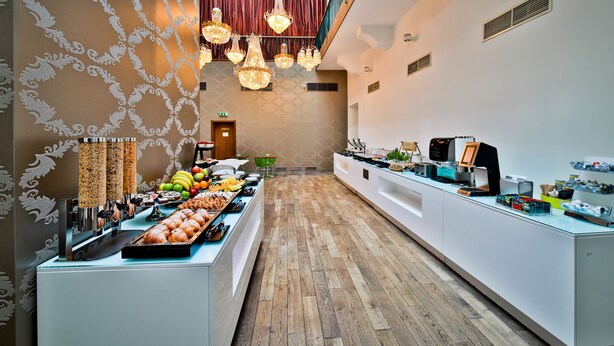 Un vestíbulo de hotel moderno con un mostrador de recepción alargado, una zona de buffet con diversas opciones de comida y una pared decorativa con un diseño.