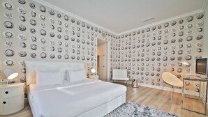 Un dormitorio moderno con una cama grande, un tapete gris y mullido, un escritorio con una silla y un televisor.
