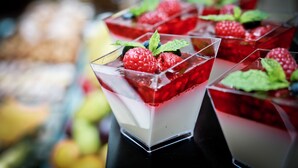 Una bandeja de postres con vasos transparentes que contienen gelatina en capas y frutos rojos frescos.