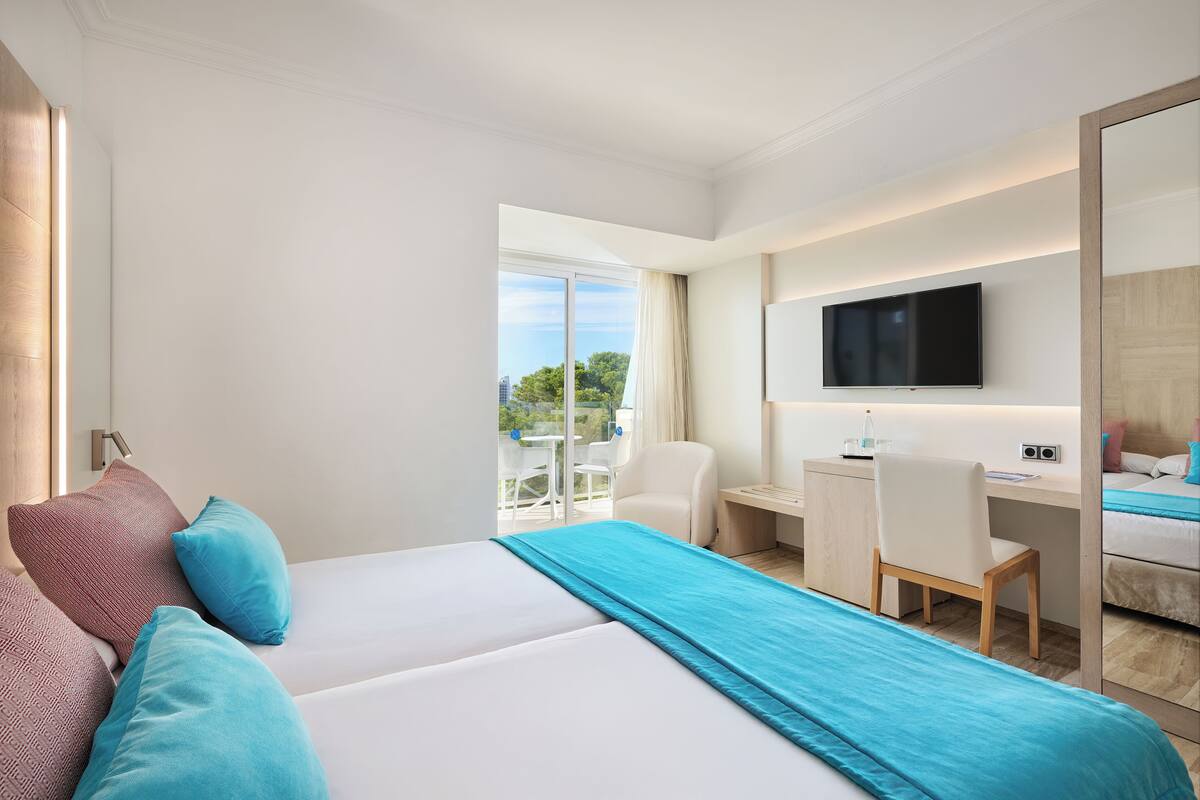 A hotel room with a large bed, a desk with a chair, a TV, and a balcony with a table and chairs.