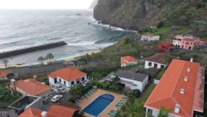 A coastal residential area with houses, a swimming pool, and a rocky coastline.