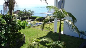 A lush garden with palm trees, a pool, and a view of the ocean.