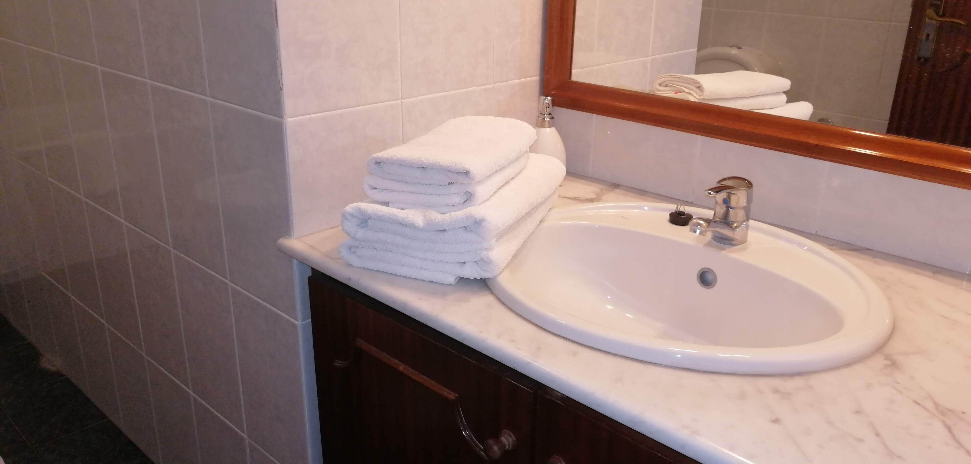 Un baño con un lavamanos blanco, un espejo y toallas blancas apiladas.