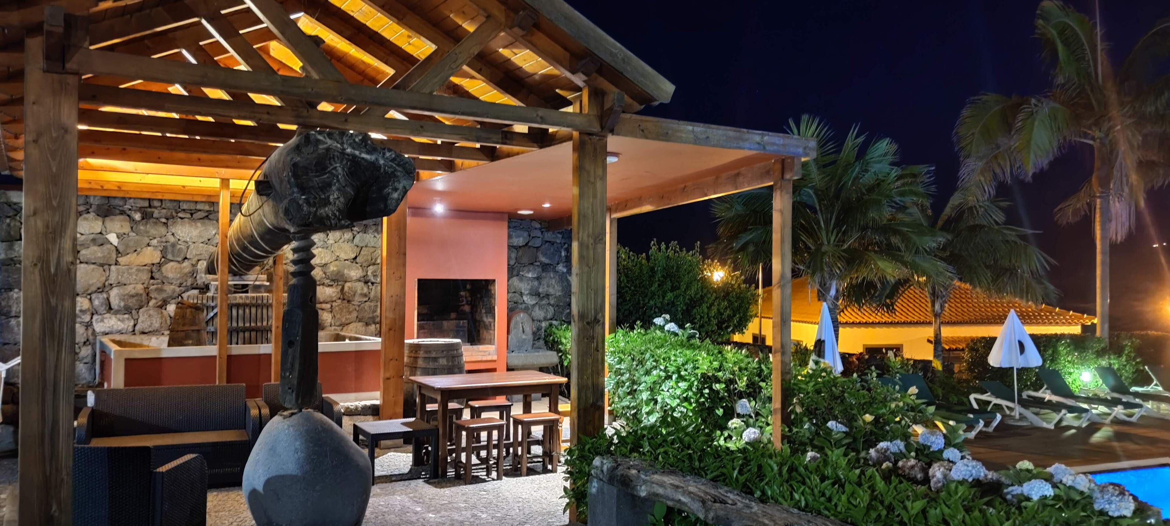 An outdoor patio with a stone wall, wooden furniture, and a pool area with lounge chairs and umbrellas.