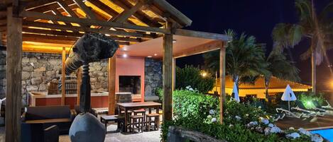 An outdoor patio with a stone wall, wooden furniture, and a pool area with lounge chairs and umbrellas.