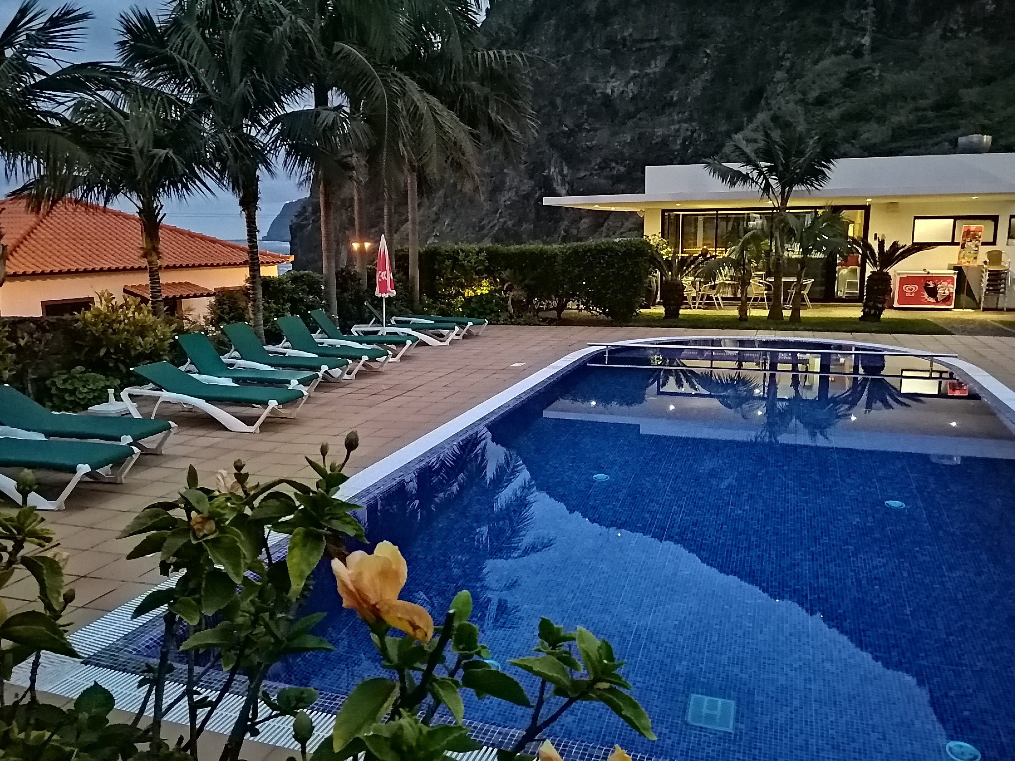 Una piscina con sillas de descanso, palmeras y un edificio al fondo.