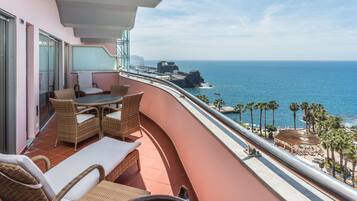 A balcony with wicker furniture, a view of the ocean, and a building in the background.