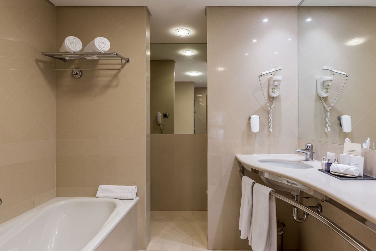 Een moderne badkamer met een bad, een wastafel met opbergruimte, een spiegel en een douchehoek.