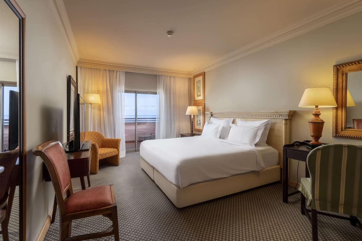 Een hotelkamer met een groot bed, een bureau, een stoel, een lamp en uitzicht op het omliggende landschap.