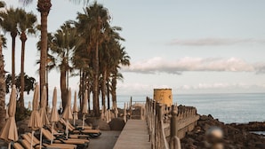 A beachside walkway lined with sun loungers and umbrellas, leading to a rocky shoreline. - Royal Savoy - Ocean Resort - Savoy Signature (Funchal)