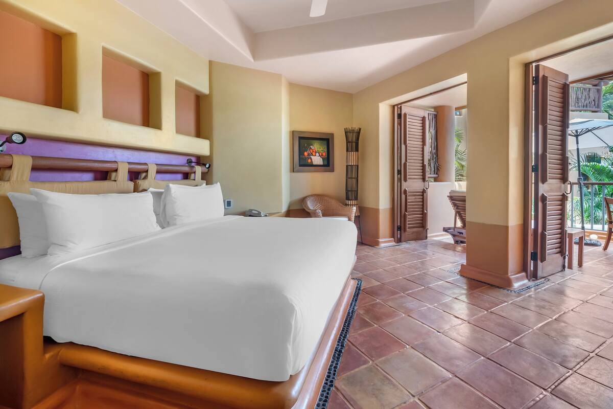 A hotel room with a large bed, a nightstand, a chair, and a view of the outdoor area.