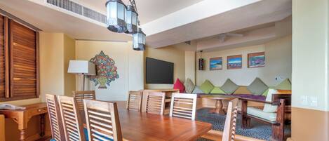 A dining area with a wooden table and chairs, a chandelier, and a television on the wall.