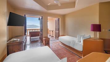 A hotel room with two beds, a desk, a TV, a lamp, and a view of the beach.
