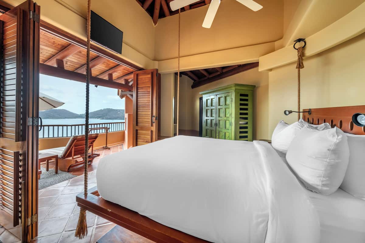 A bedroom with a bed, a view of the sea, a wooden ceiling, and a green cabinet.