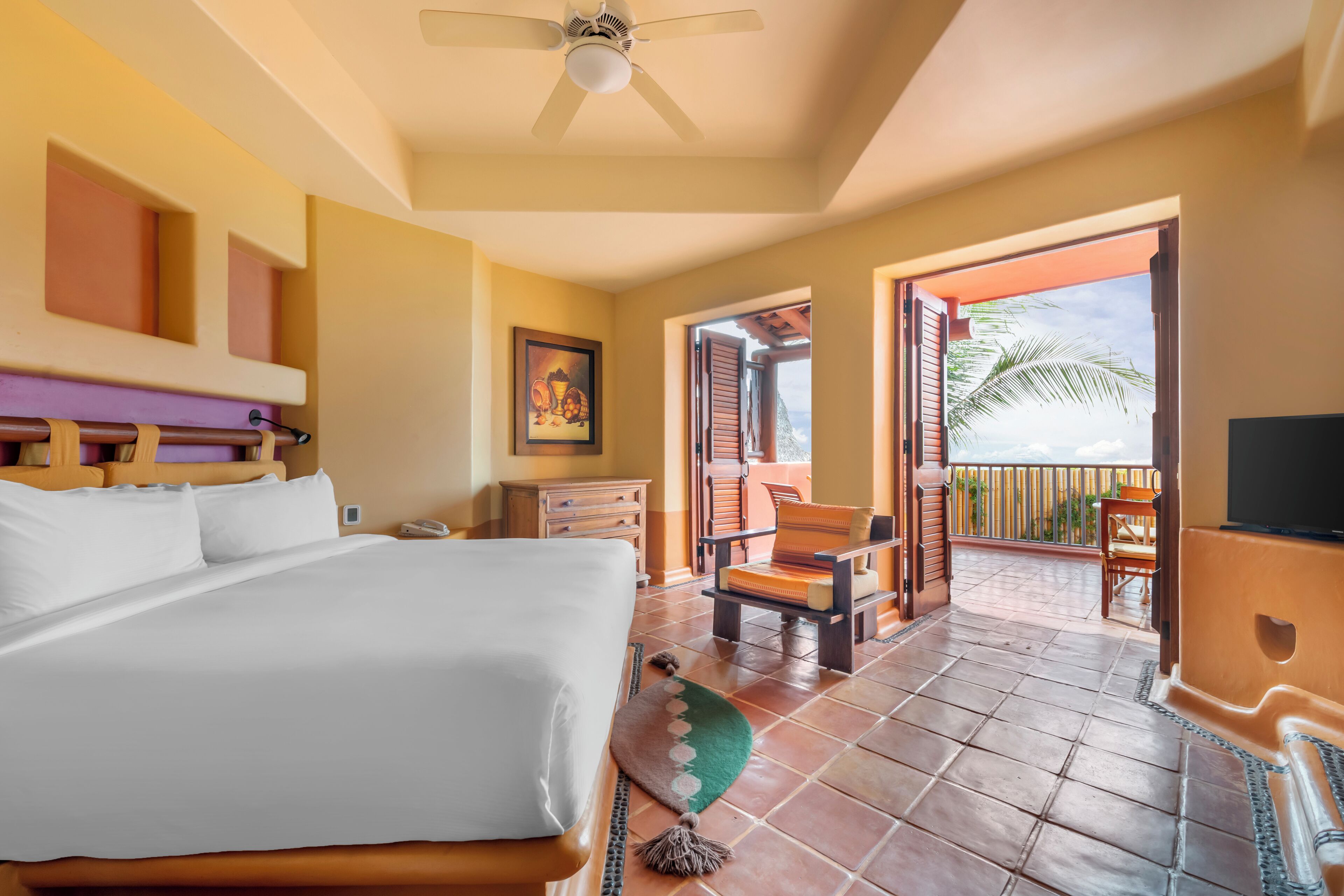 Une chambre d’hôtel avec un lit, un bureau, une chaise, une télévision et un balcon avec vue.