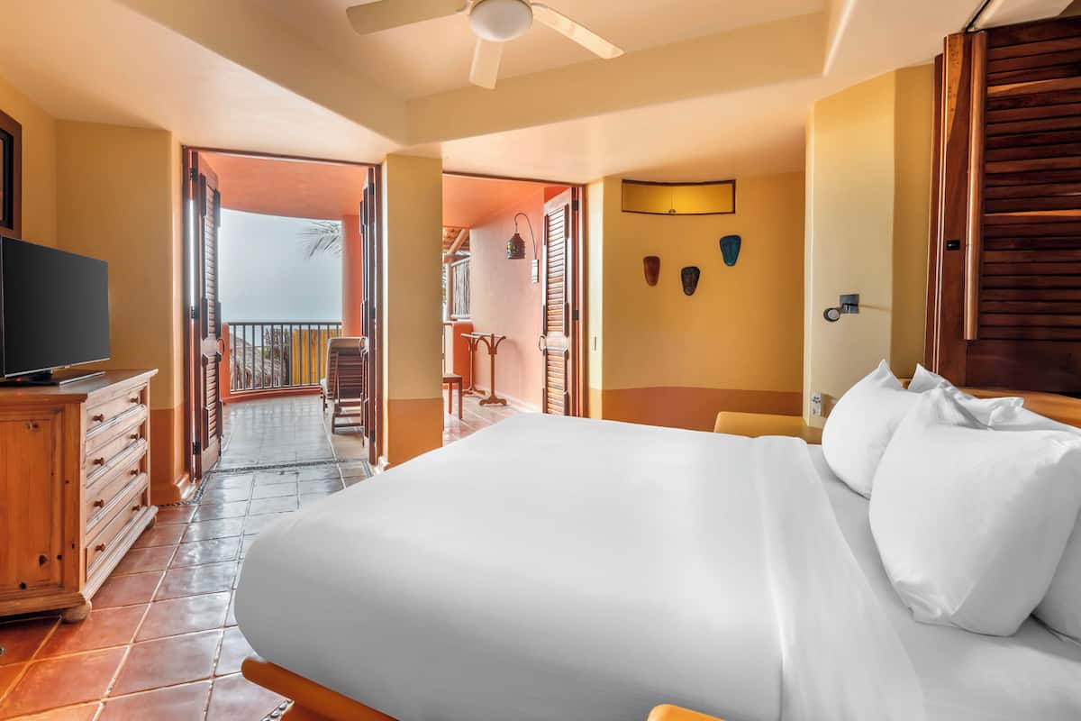 A hotel room with a large bed, wooden furniture, a TV, and a balcony with a view.