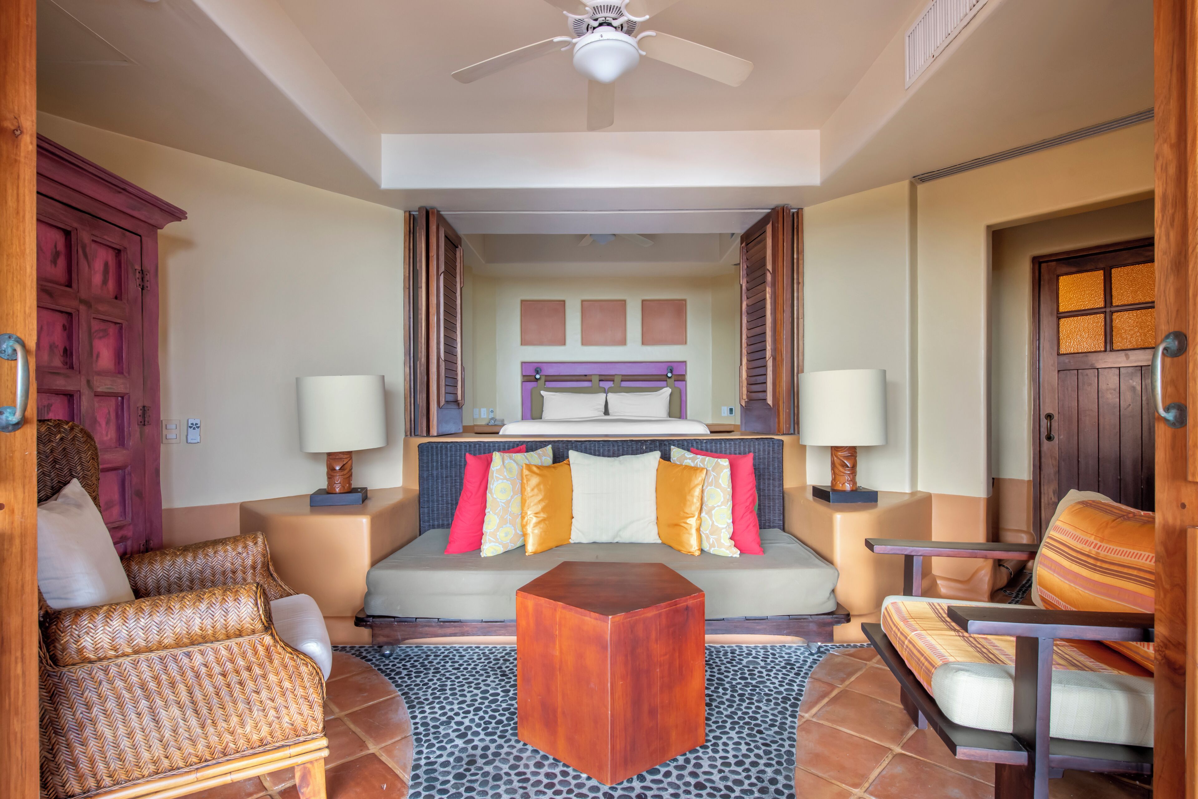 Una habitación de hotel con una cama, dos sillas, una mesa de centro de madera y un ventilador de techo.
