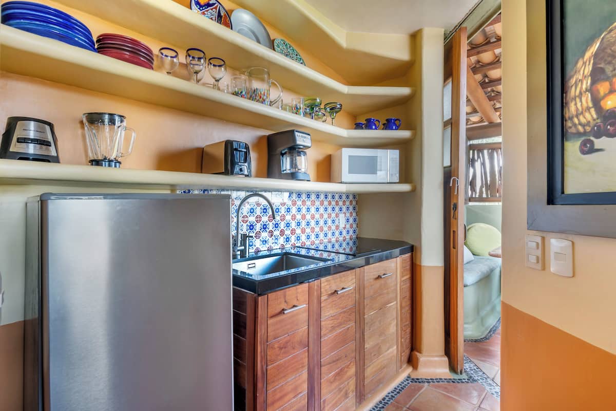 A compact kitchen with a stainless steel refrigerator, wooden cabinets, and a tiled backsplash.
