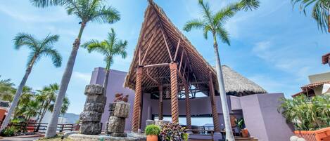 A resort with a thatched-roof pavilion, palm trees, and a stone fountain.