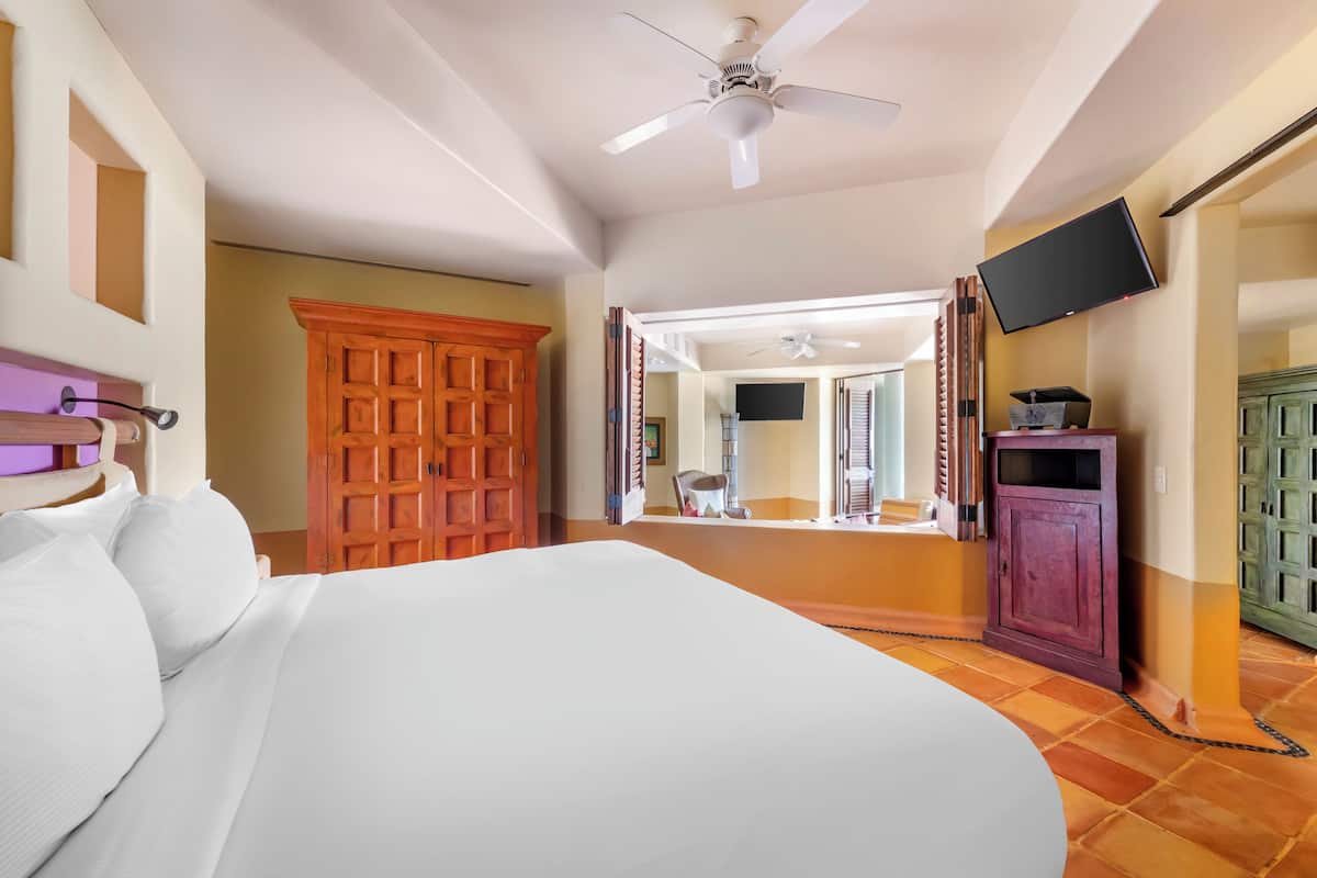 A hotel room with a large bed, a ceiling fan, a TV mounted on the wall, and a wooden wardrobe.