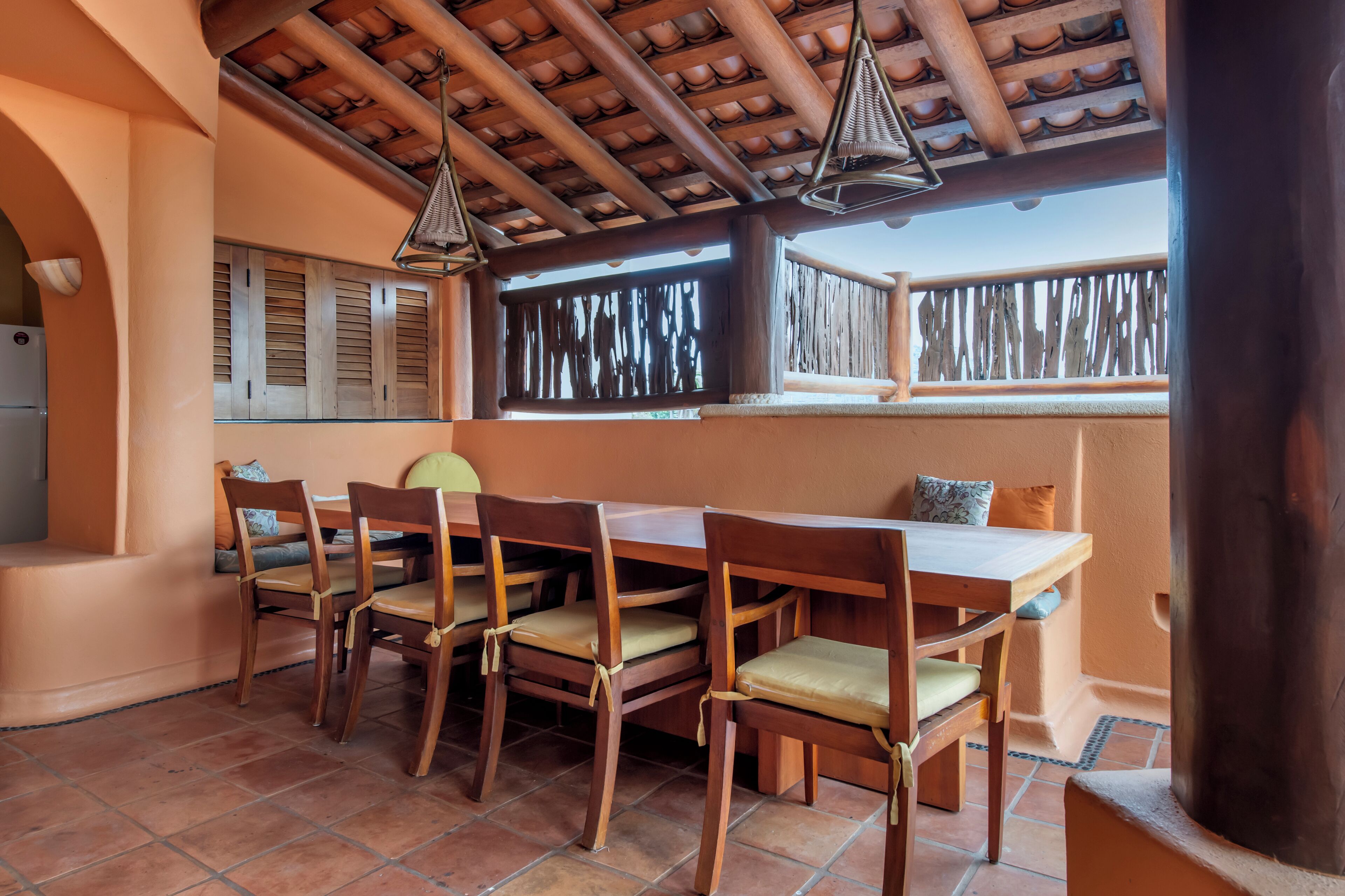 A dining area with a wooden table and chairs, a tiled floor, and a ceiling with exposed beams.