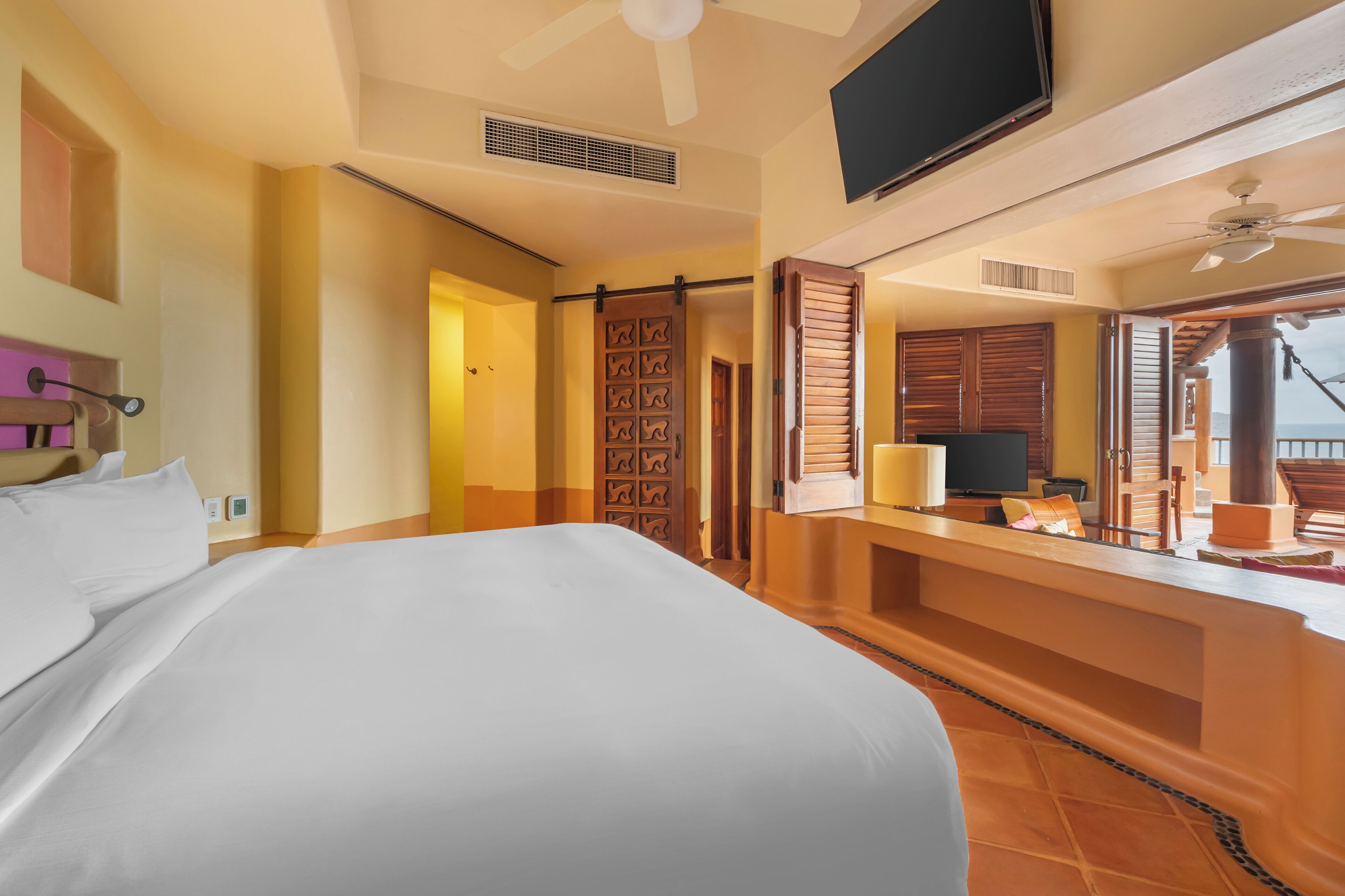 Habitación de hotel con una cama grande, televisión, escritorio con silla y balcón con vistas.