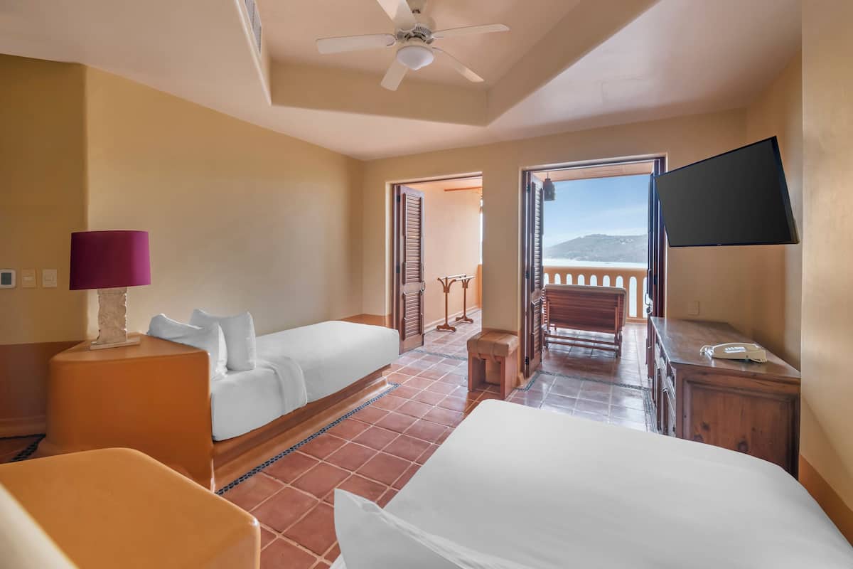 A hotel room with two beds, a ceiling fan, a TV, and a balcony with a view.