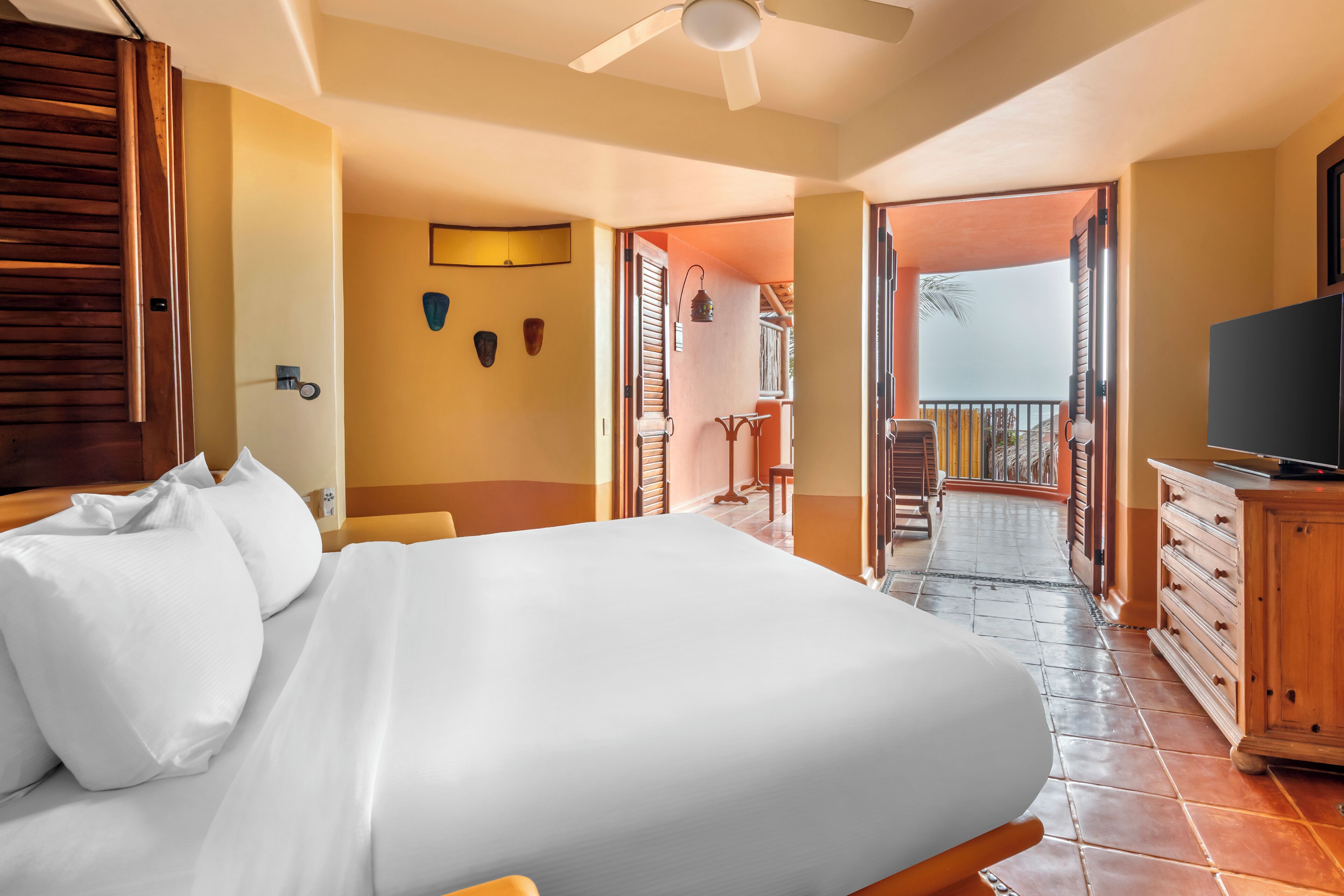 Quarto de hotel com cama, mobiliário de madeira, televisão e varanda com vista.