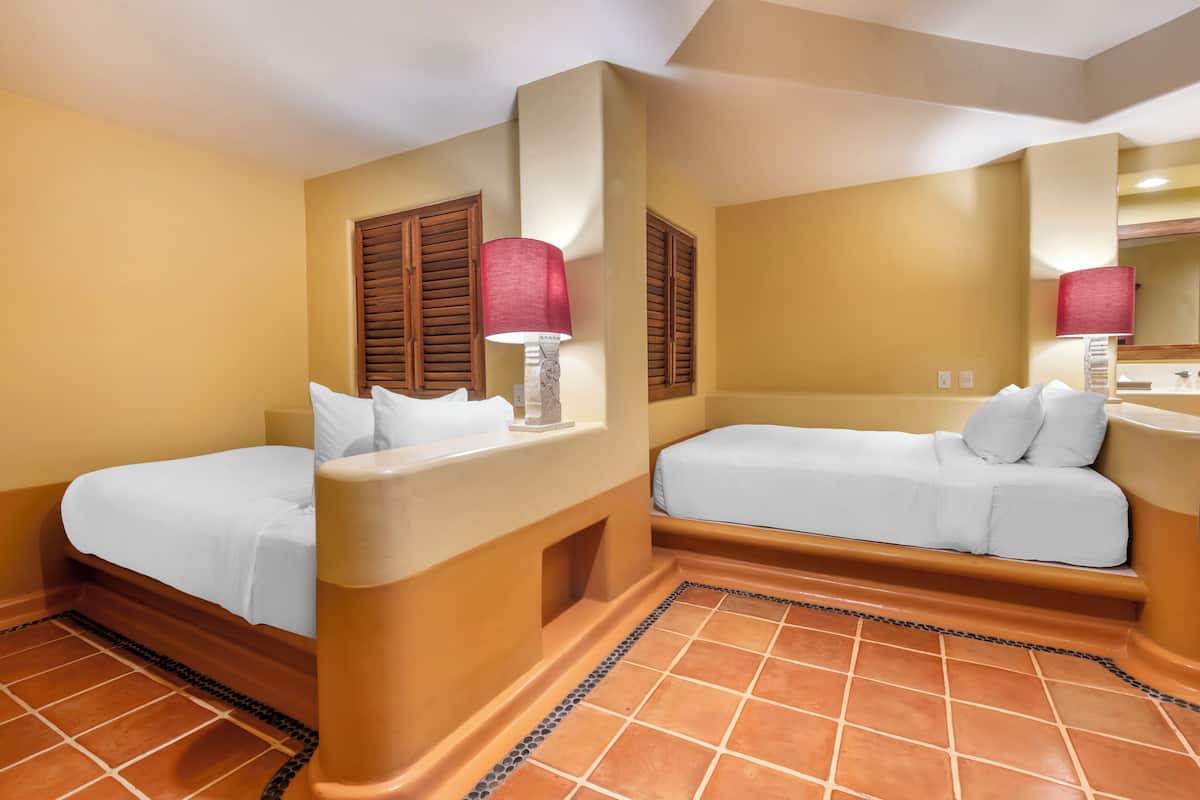 A hotel room with two beds, a nightstand, a lamp, and a tiled floor.