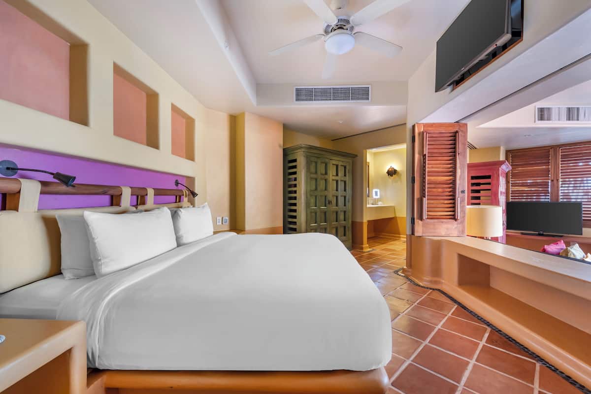 A hotel room with a bed, a ceiling fan, a TV, and a bathroom visible through an open door.