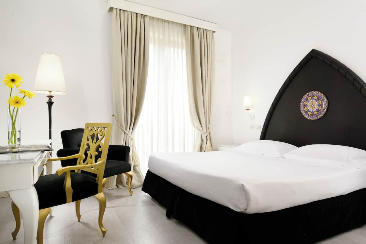 A hotel room with a bed, a desk with a lamp, a chair, and a window with curtains.