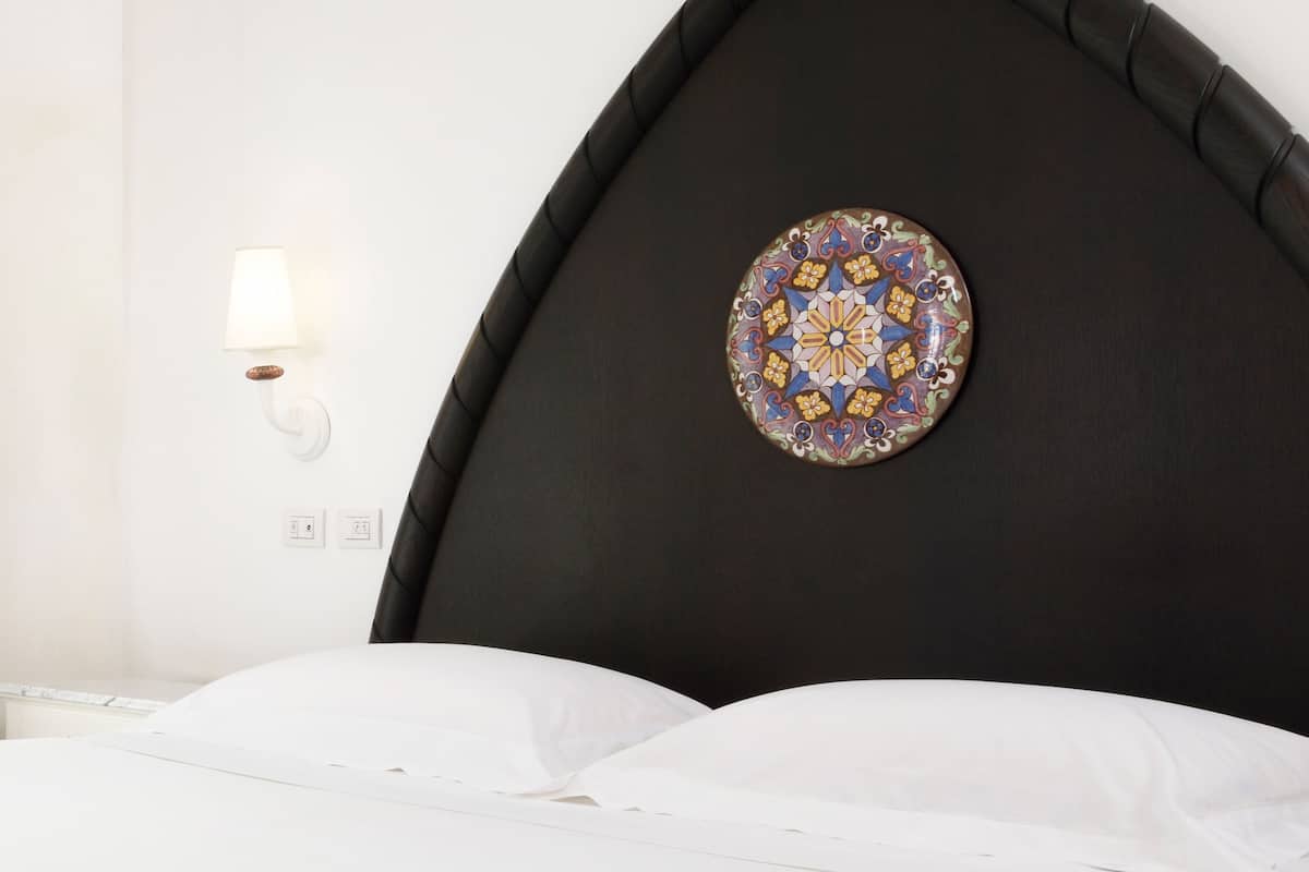 A bed with white linens, a dark headboard, and a decorative wall plate.