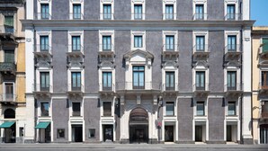 A multi-story building with a central entrance labeled "PALACE CATANIA." It features a symmetrical facade with evenly spaced windows and balconies. - Palace Catania | UNA Esperienze (Catania)