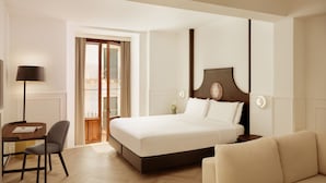 A hotel room with a large bed, a desk with a chair, a sofa, and a lamp. - Palace Catania | UNA Esperienze (Catania)