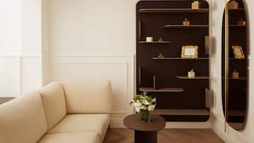 Uma sala de estar moderna com um sofá bege, uma mesa lateral redonda com um vaso de flores e uma estante de madeira escura com objetos decorativos.