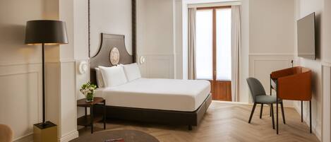 A hotel room with a bed, bedside table, lamp, chair, and a small round table with a book.