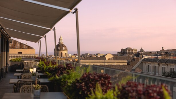 A terrace with outdoor seating, a view of historic buildings, and a dome structure in the distance. - Palace Catania | UNA Esperienze (Catania)