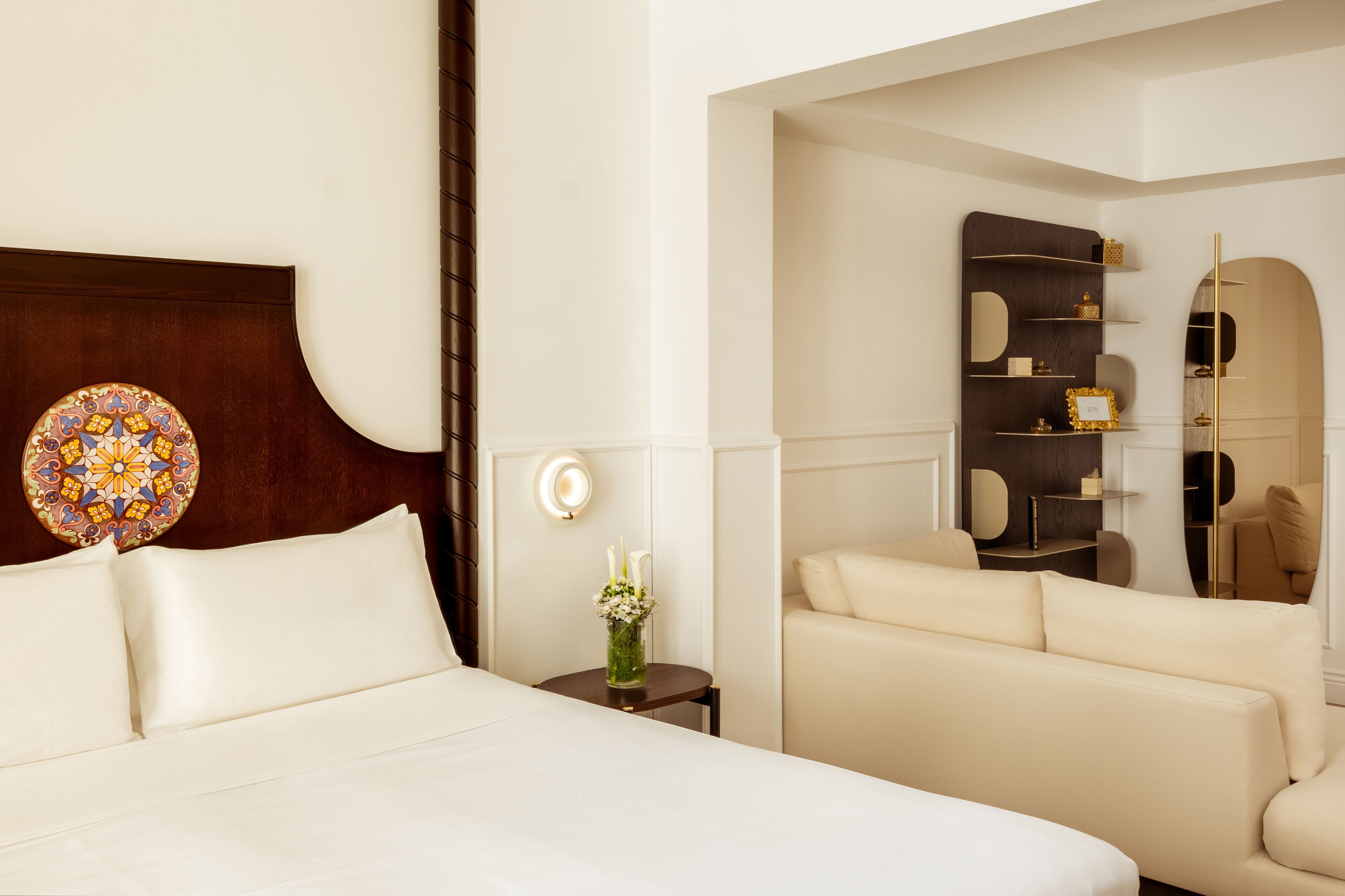 Habitación de hotel con una cama grande, una mesita con un florero, un sofá y un mueble decorativo en la pared.